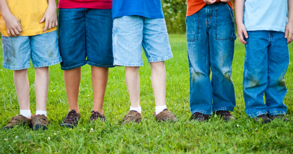 A group of young children standing in a sunny field, each sporting vibrant green grass stains on their knees after an adventurous playtime.