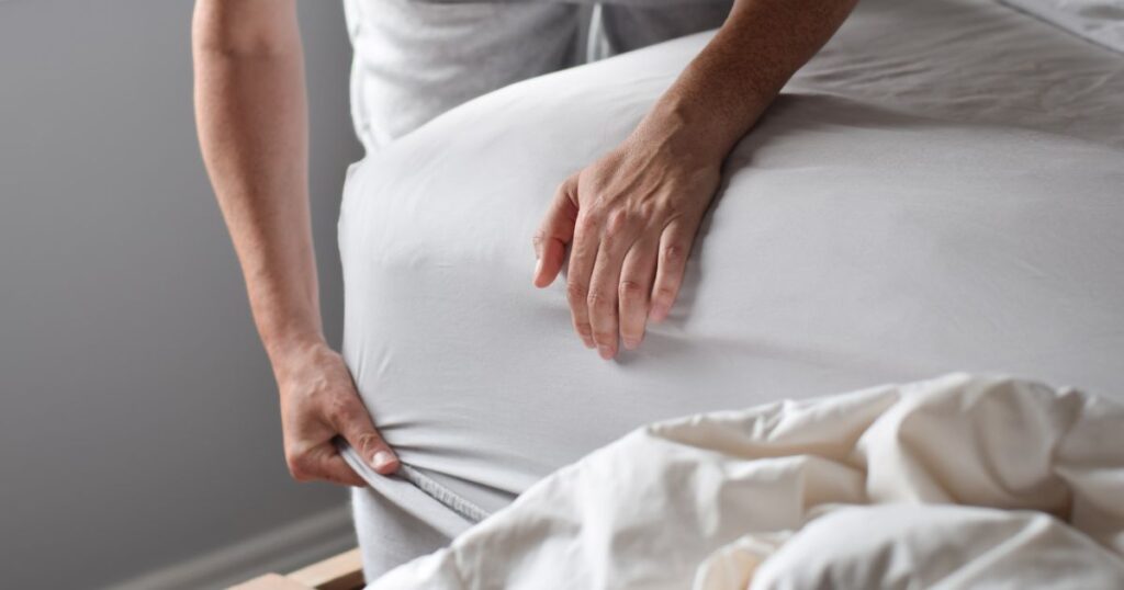 Hands placing a fitted sheet onto a bed, demonstrates the importance of properly folding.