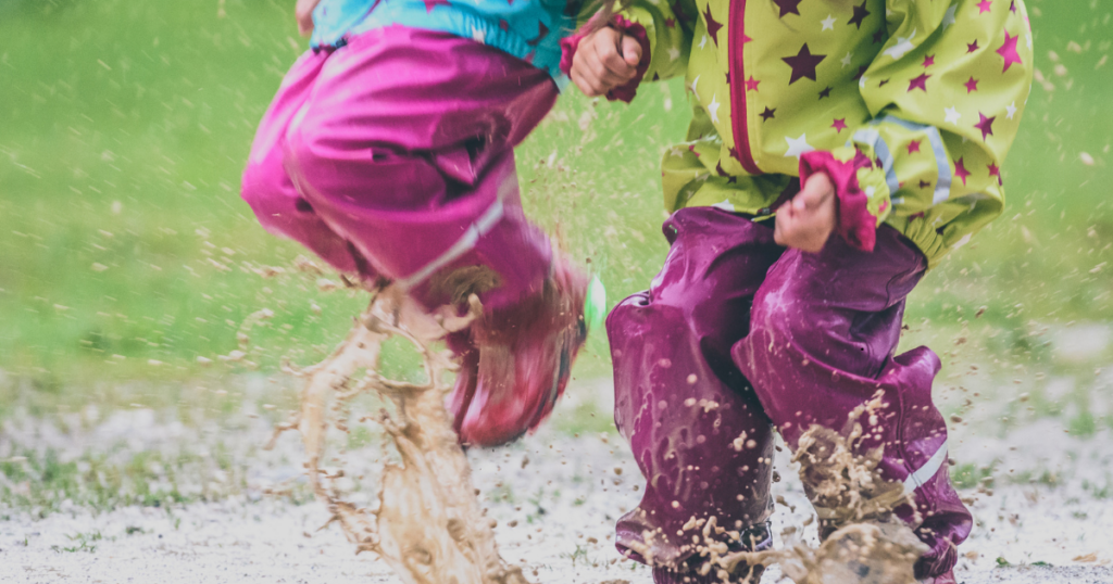 Kids playing in the rain, splashing in puddles with damp and musty clothes soaked in muddy rainwater, showing why laundry during the spring storm season is important.